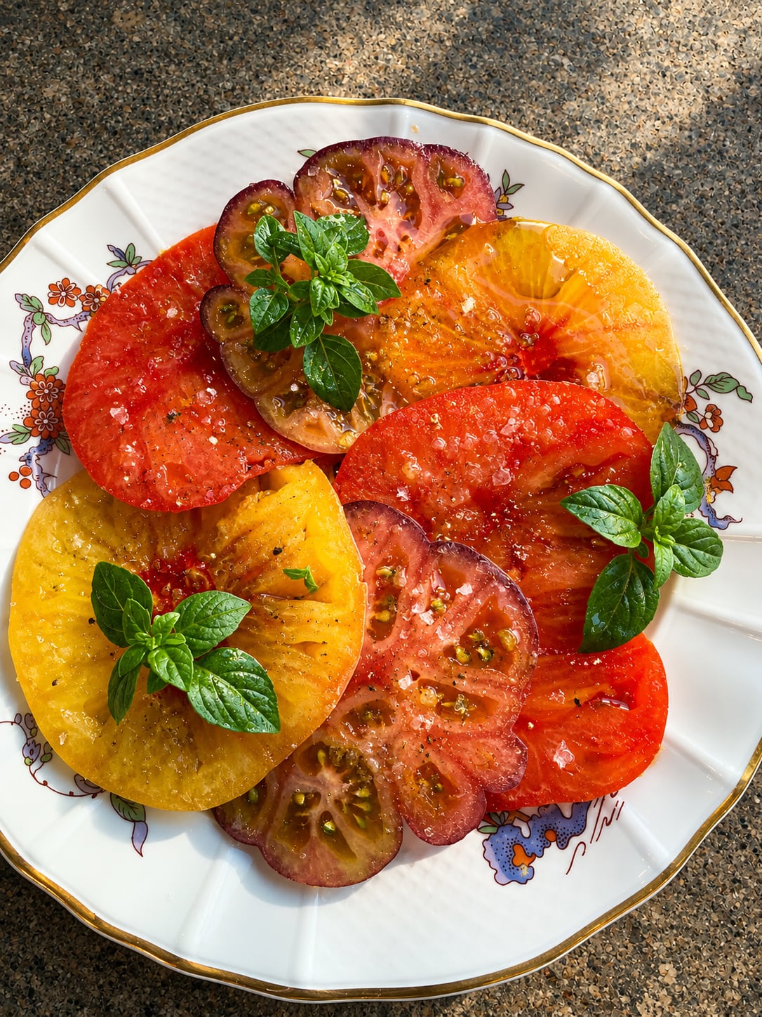 Heirloom tomato carpaccio with basil on a gold-rimmed plate