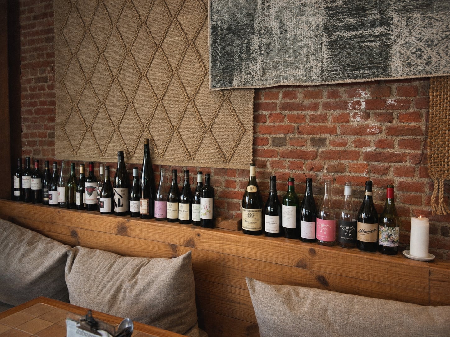 Wine bottles lined along the shelf above the banquette, against brick and woven rugs