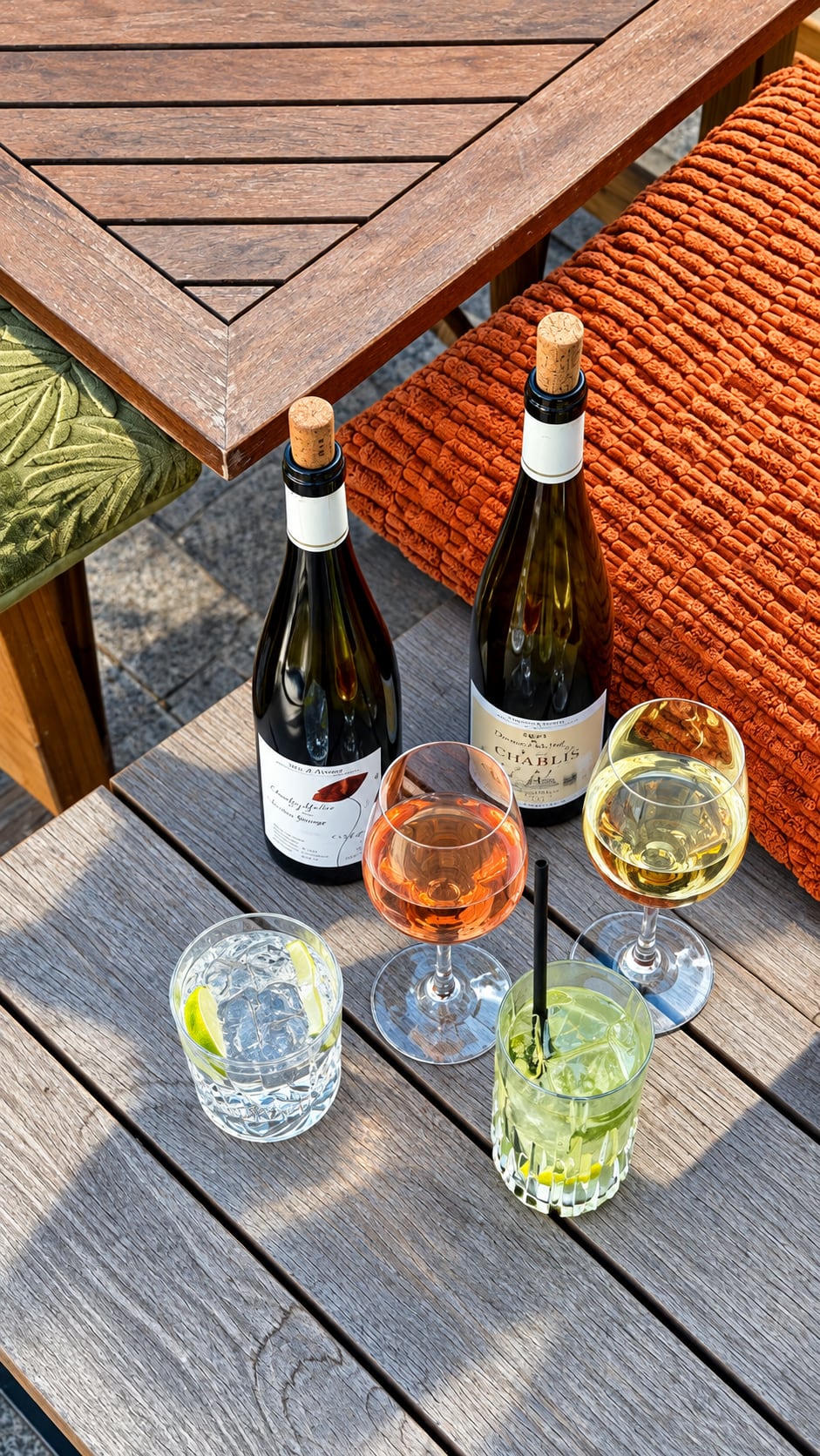 Two bottles of white wine, glasses and a gin and tonic on a sunny terrace table